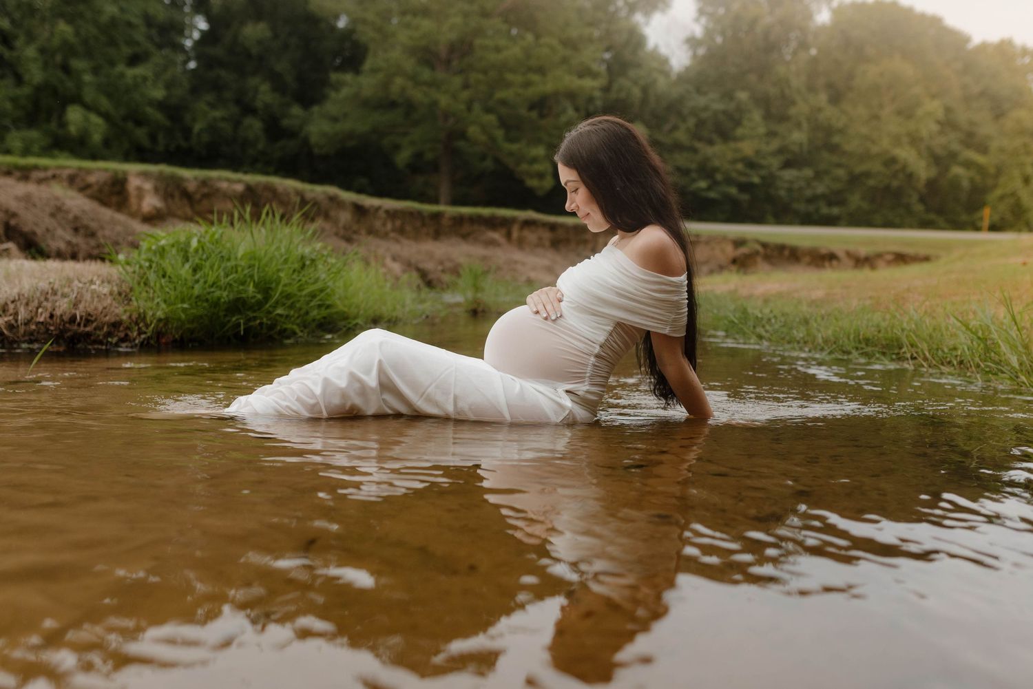 Ethereal water maternity photos with flowing white dress in golden sunlight.