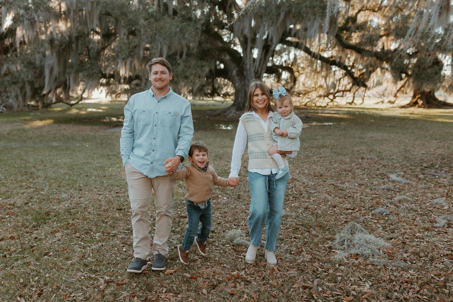 A family group poses together under moss-draped oak trees on an autumn day.