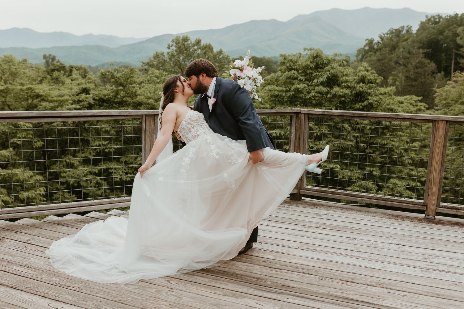 Elegant wedding portraits on wooden deck with mountain scenery.