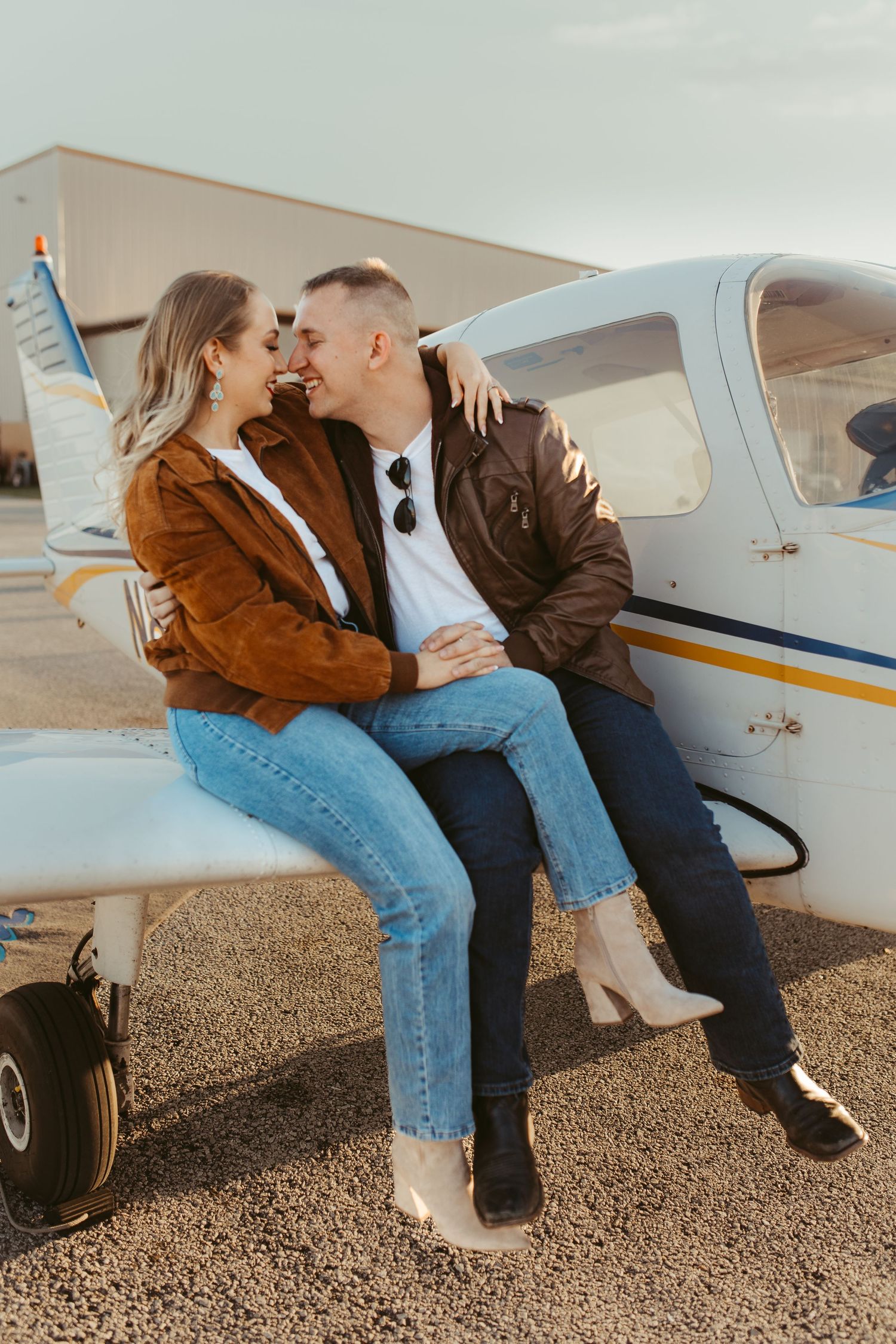 Couple in casual wear sitting on aircraft wing sharing intimate moment.