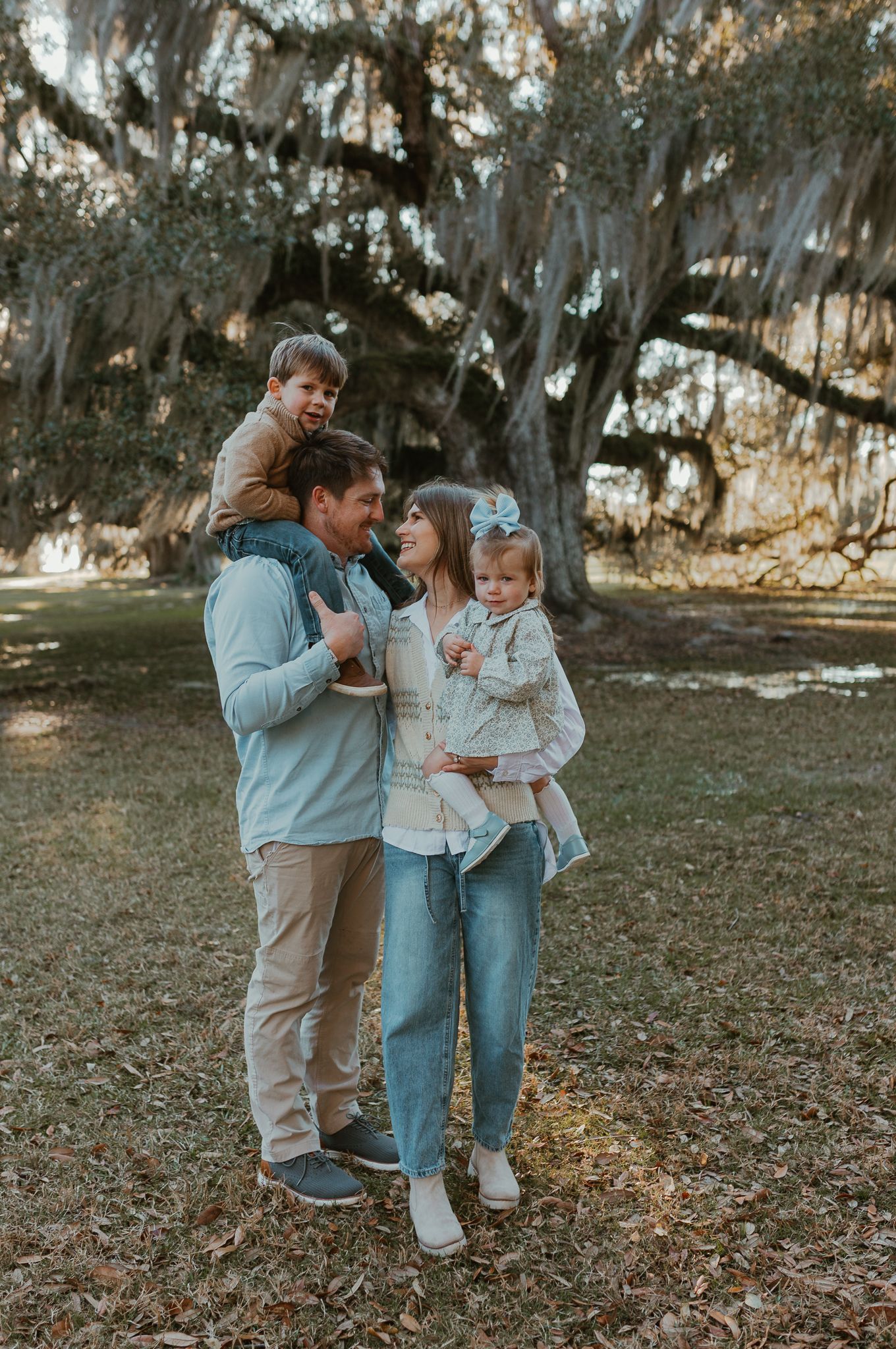 Family enjoying a tender moment together under moss-draped trees in a park.
