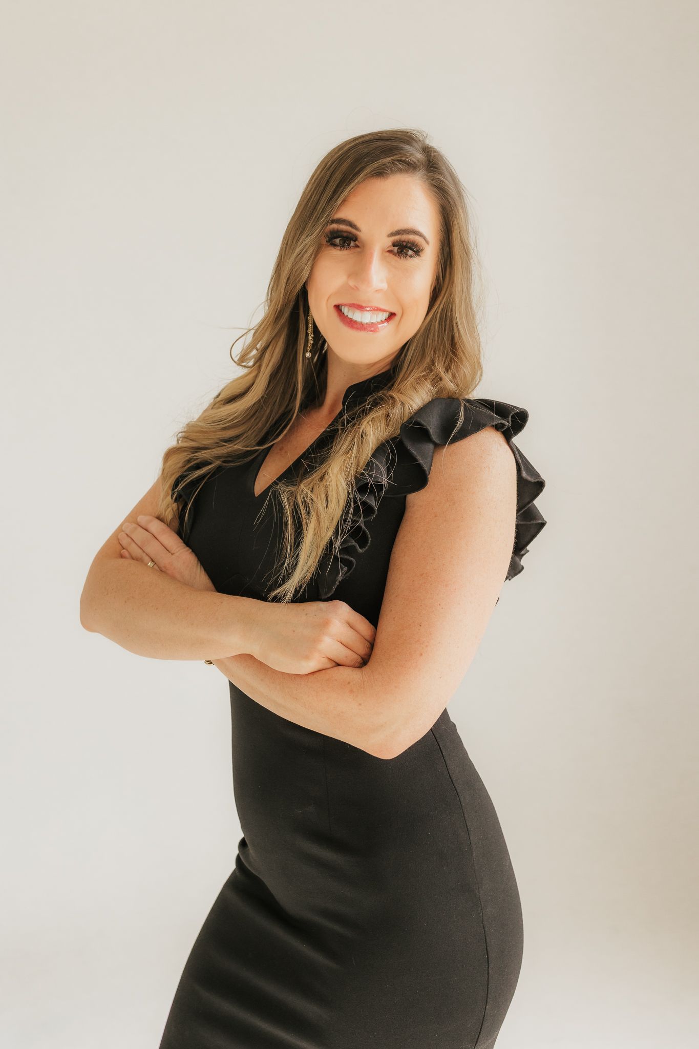 Professional portrait of a woman in a black dress with ruffled sleeves against a light background.