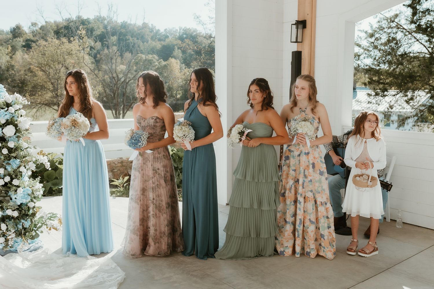 Wedding party in pastel blue and sage dresses gathered on outdoor terrace.