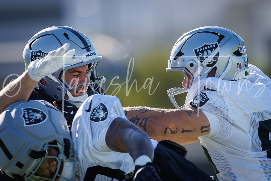 Two Las Vegas Raiders players in silver helmets engage in blocking drill during NFL training camp practice.