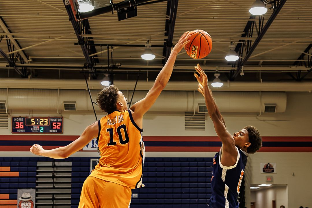 Two basketball players compete for the ball, player #10 in orange jersey attempts a shot while defender contests.