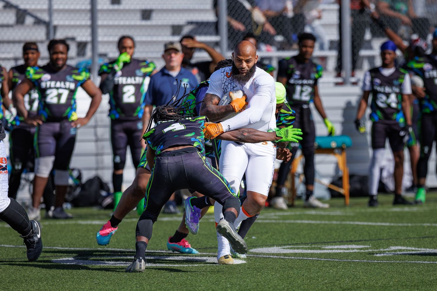 Players in green Stealth jerseys compete in an intense flag football game on a turf field during a sunny day.