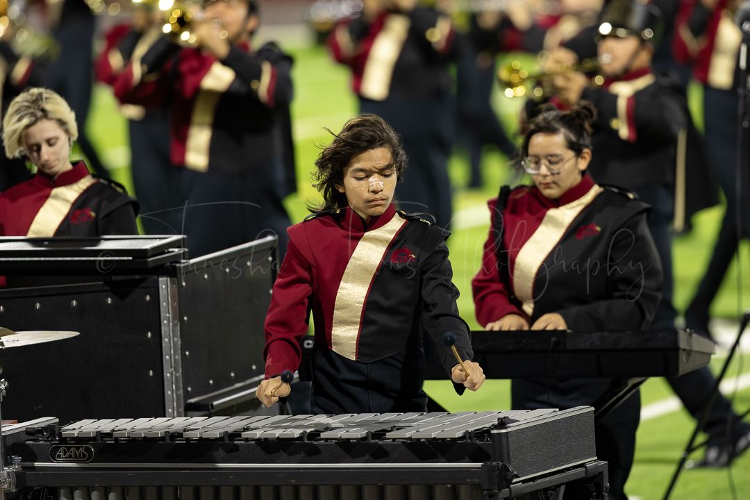 Musicians in marching band uniforms perform at keyboard instruments during halftime show.