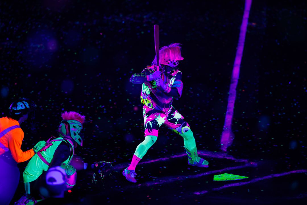 Person in neon UV-reactive outfit swinging a bat under black light at a glowing neon party event.