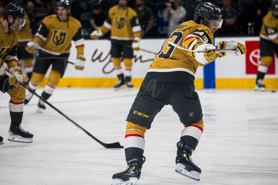 Hockey player in gold Vegas Golden Knights jersey takes a shot during gameplay on ice.