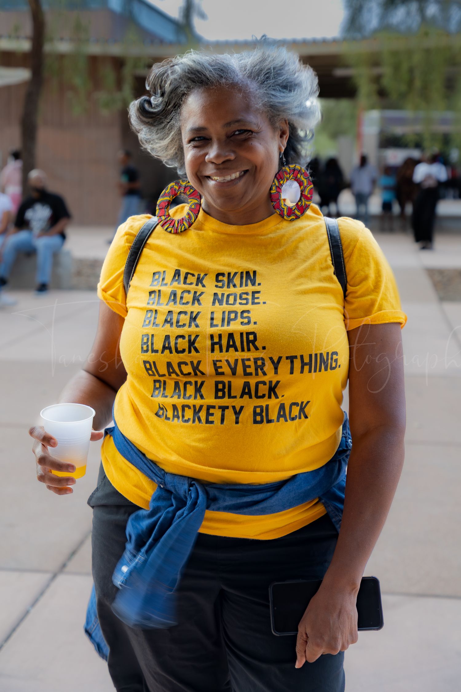 Person wearing yellow t-shirt with text about black identity at outdoor event.