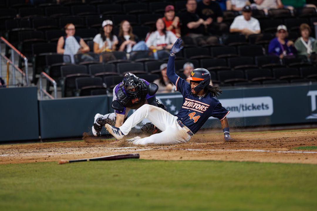 Baseball player slides into home plate as catcher attempts the tag during a night game.