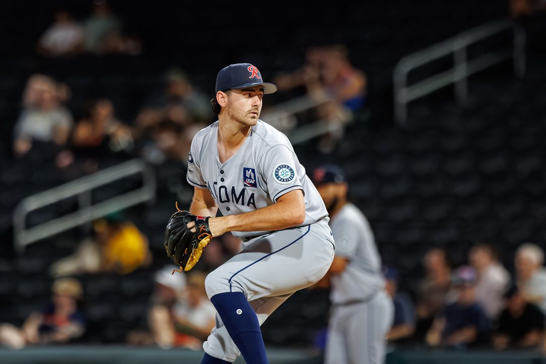 Tacoma Rainiers pitcher in gray uniform winds up for a pitch during a minor league baseball game at night.