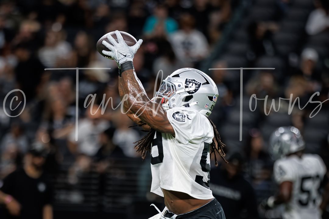 Football player in white Raiders jersey catches a pass during a night game at Allegiant Stadium.