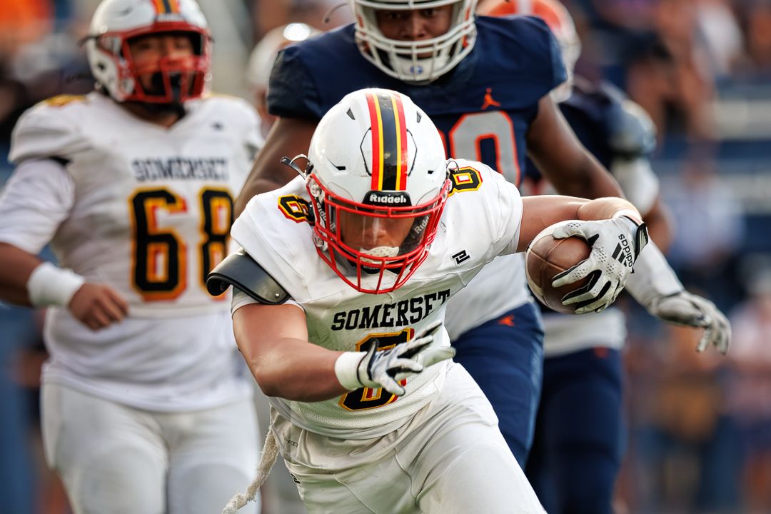 Somerset football player carries the ball during a competitive high school football game on a sunny day.