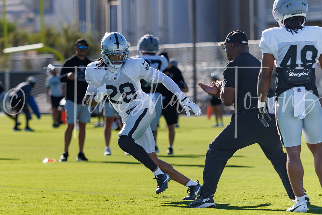 Raiders player #28 runs a drill during NFL training camp practice on a sunny day.