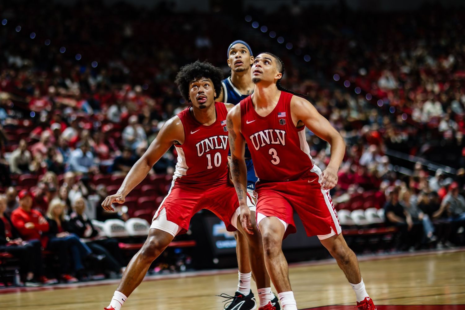 UNLV basketball players in red jerseys competing on court during a college basketball game.