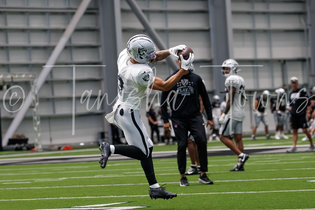 Raiders player catches football during indoor practice facility training session wearing black and white team uniform.