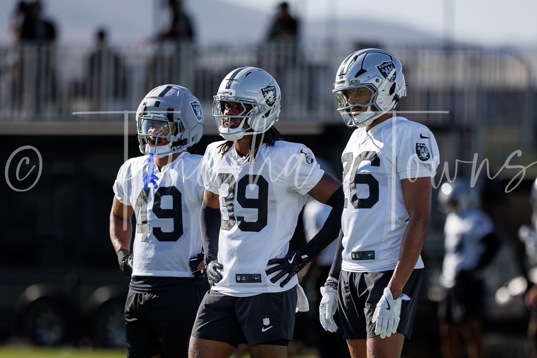 Three Las Vegas Raiders players stand together on field during training camp practice.