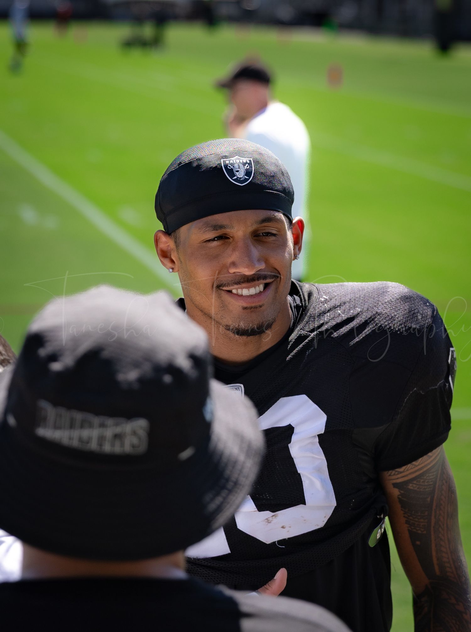 Raiders player in black jersey and team cap interacts with fans during training camp.