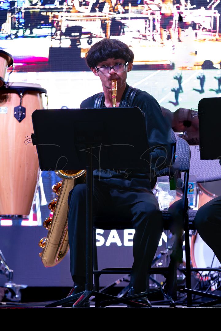 Silhouetted musicians with instruments and music stands on stage during a performance.