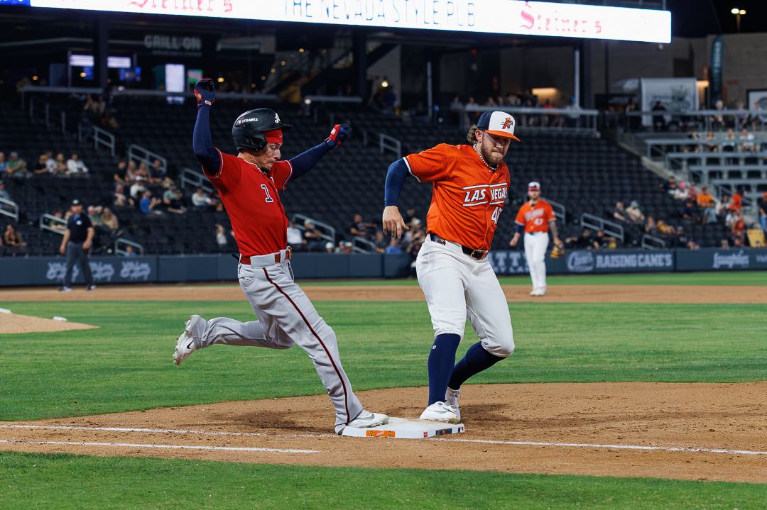 A baseball player races to first base as the first baseman stretches to catch the ball during a MiLB game.