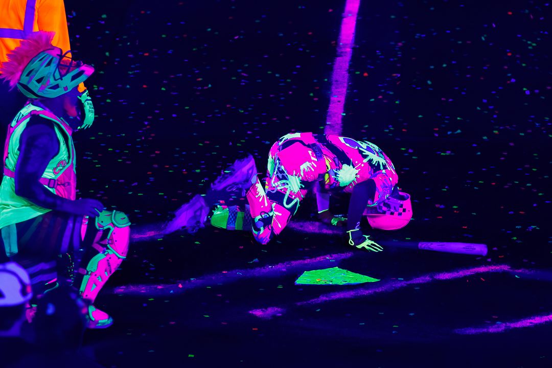 Two performers in neon UV-reactive costumes dance under black light at a vibrant glow party event.