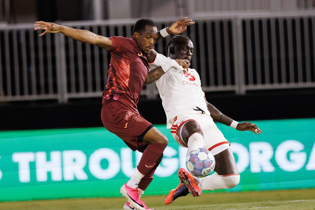 Two soccer players compete for the ball in an intense aerial duel during a night match.