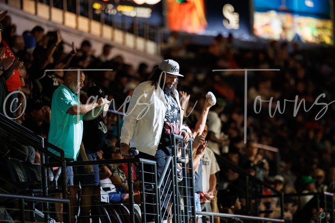 Crowd of fans standing in stadium bleachers during a nighttime sporting event.