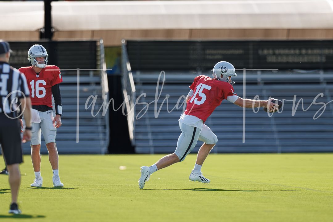 Football players in red and white jerseys practice drills on a green field during a Las Vegas Raiders training camp.