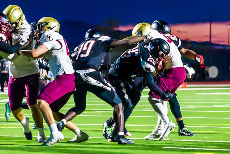 Football players engage in blocking and tackling during competitive night game.