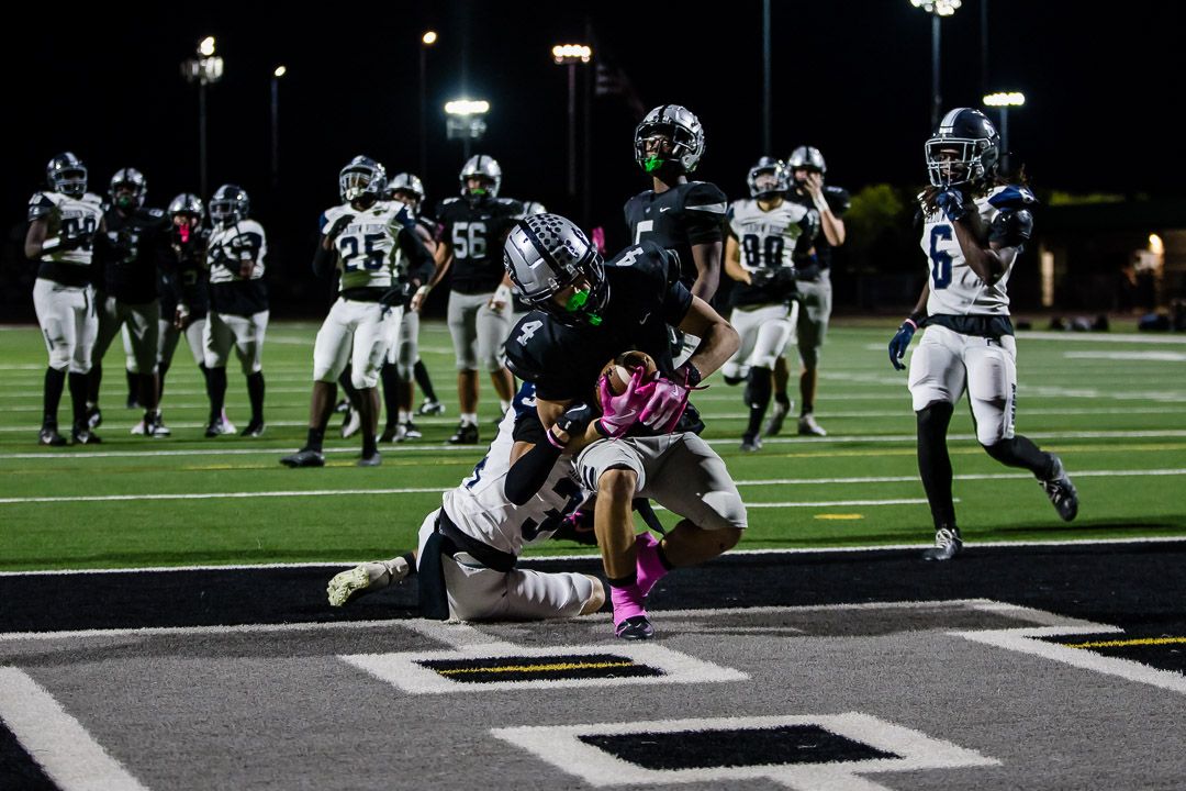 Football players engage in a scrimmage play on a brightly lit field at night.
