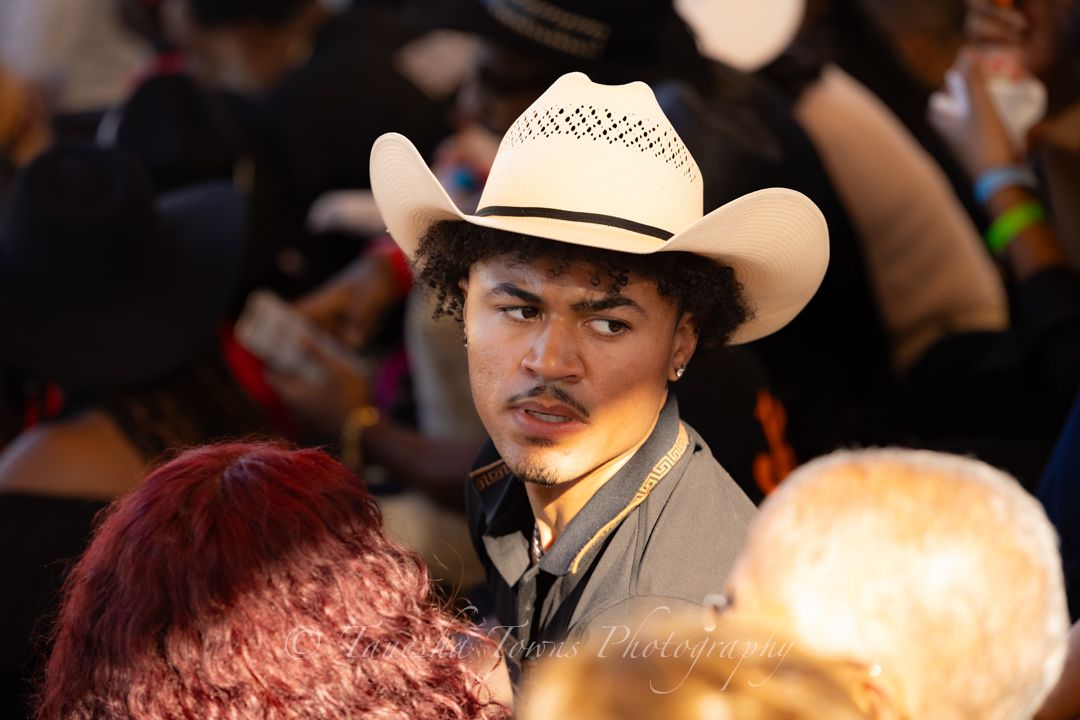People in cowboy hats gathered at a western-style event with festive lighting and decorations.