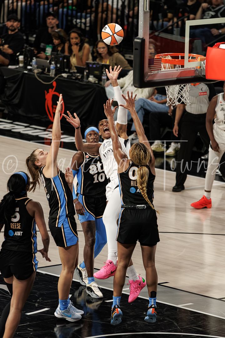 WNBA players compete for a layup shot during an intense basketball game, with defenders raising arms to block.