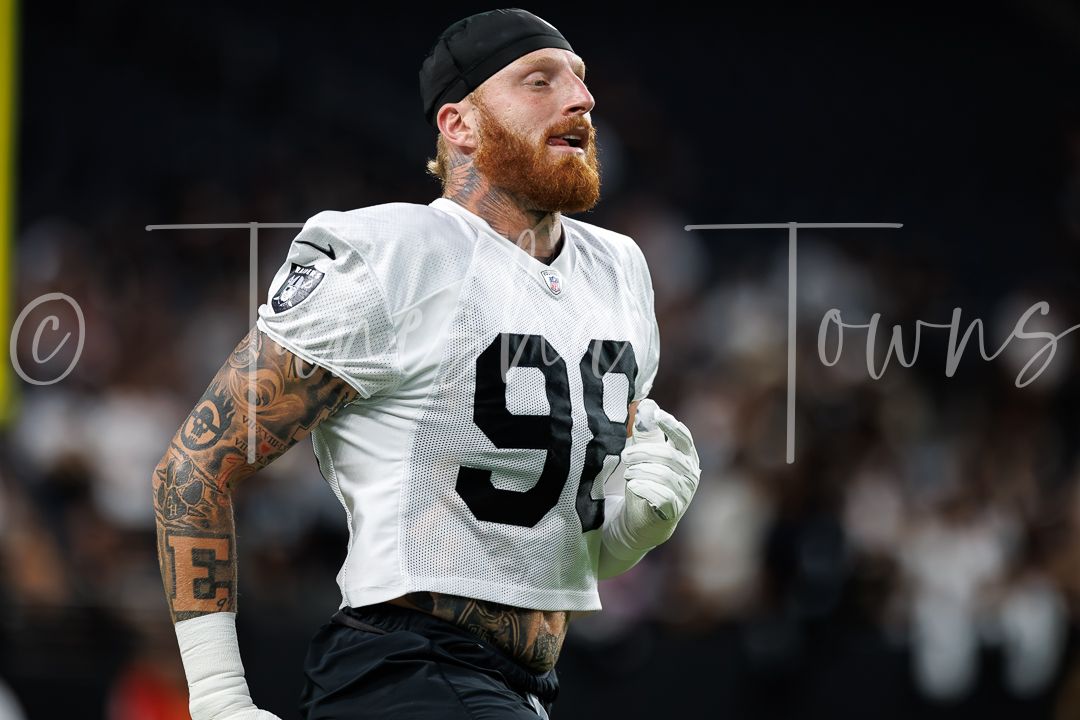 Tattooed Las Vegas Raiders defensive end wearing number 98 white jersey jogs on the field at Allegiant Stadium.