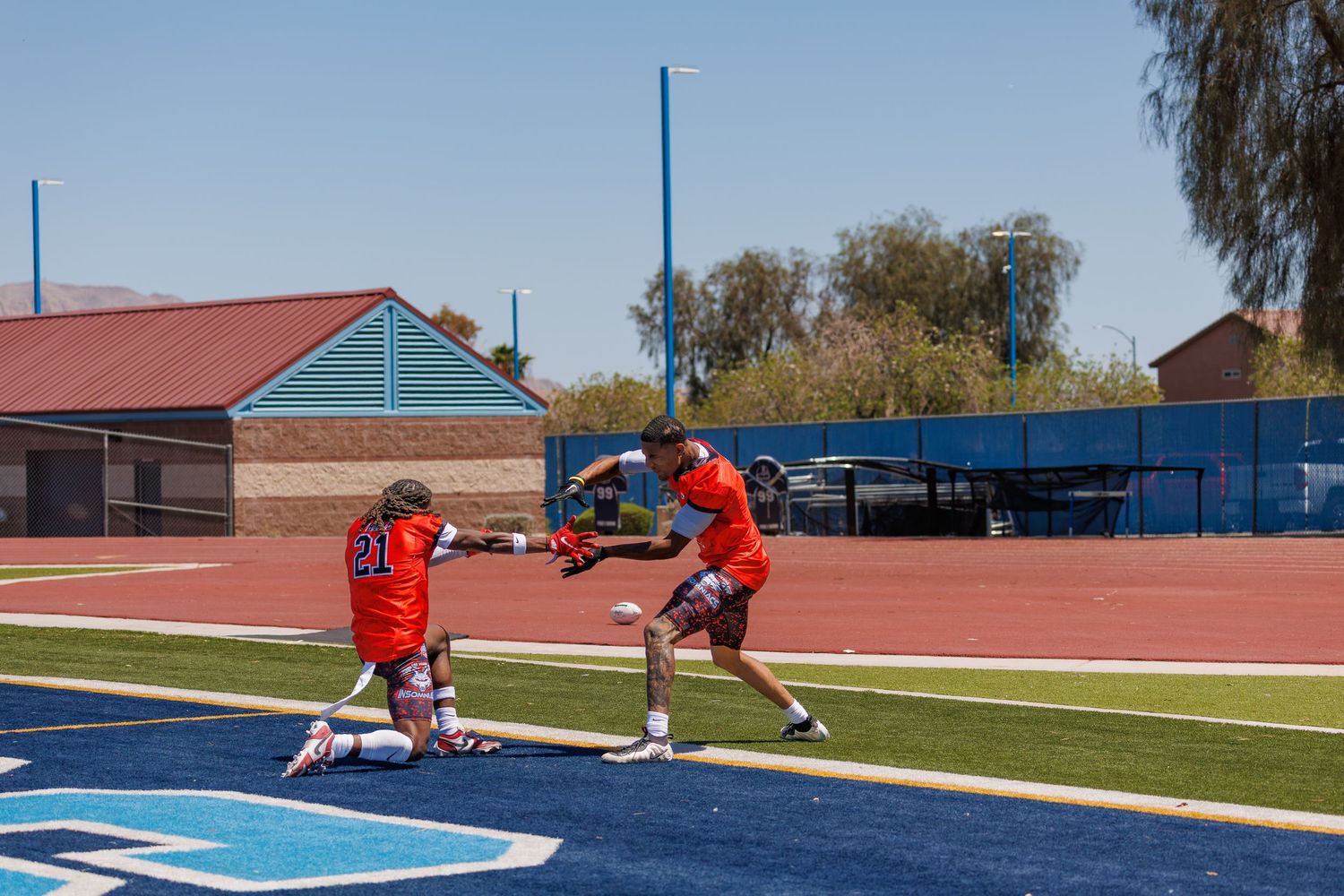 Two lacrosse players practice passing drills on a blue turf field during a sunny outdoor training session.