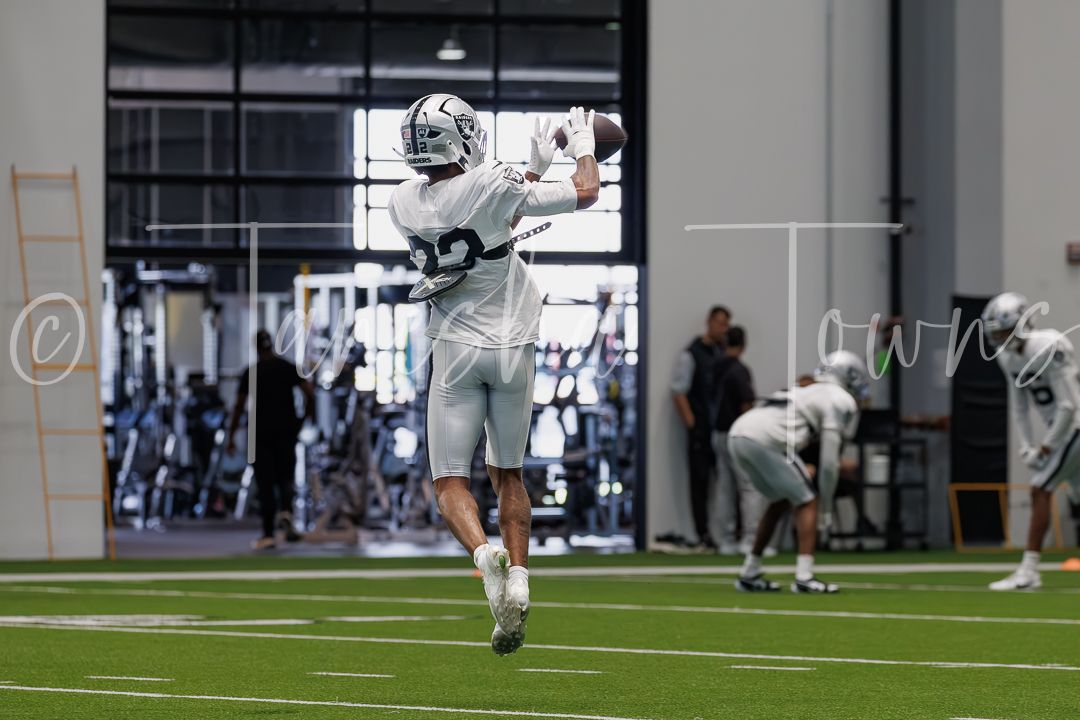 Football player in gray uniform catching a pass during an indoor practice session on a green turf field.