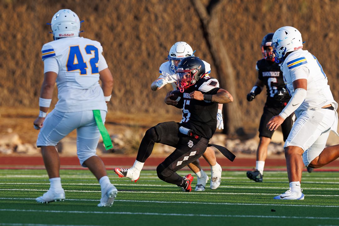 Football player in dark uniform breaks through defenders in blue and white jerseys during a competitive game.