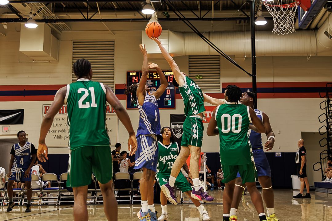 Basketball players in green and blue uniforms compete for a rebound during an indoor basketball game.