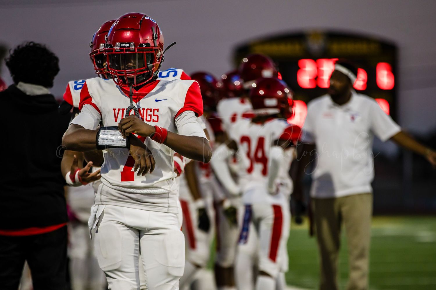Football player in red helmet and white uniform stands on sideline during nighttime game.