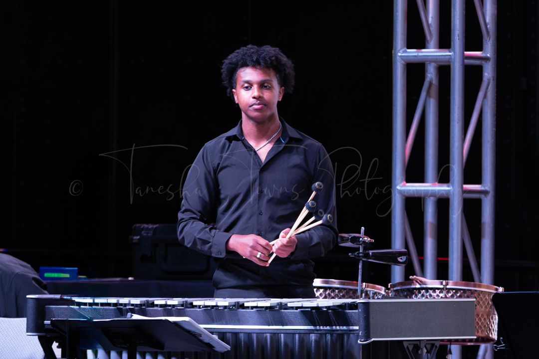 Musicians perform on stage with keyboards and instruments during a dark nighttime concert.
