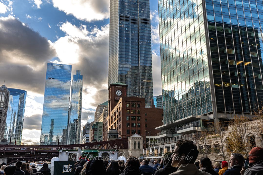 Modern glass skyscrapers reflect clouds and sunlight along Chicago's riverfront on a bright afternoon.