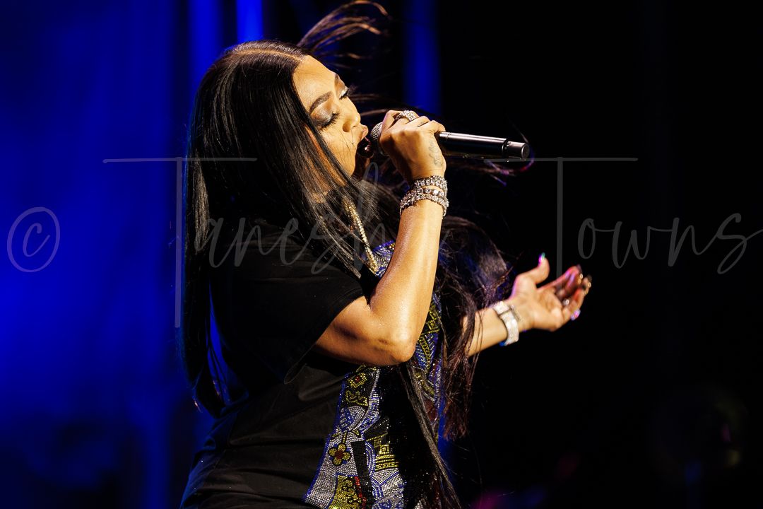 Female vocalist singing passionately on stage, wearing black top with colorful graphic detail and silver bracelets.