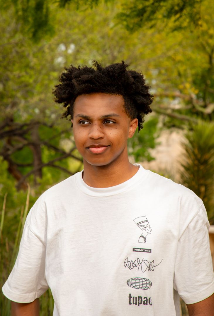 Person modeling a casual white t-shirt with small logo design in an outdoor garden setting.