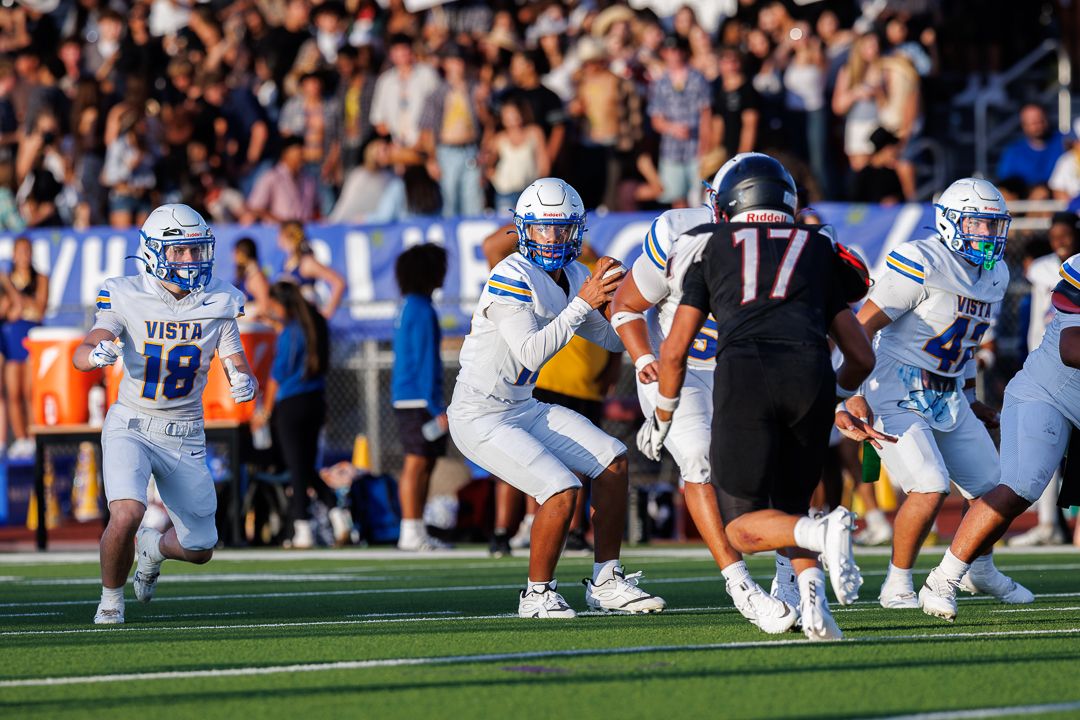 Vista football players in white uniforms compete on field, number 17 opponent faces defenders under stadium lights.