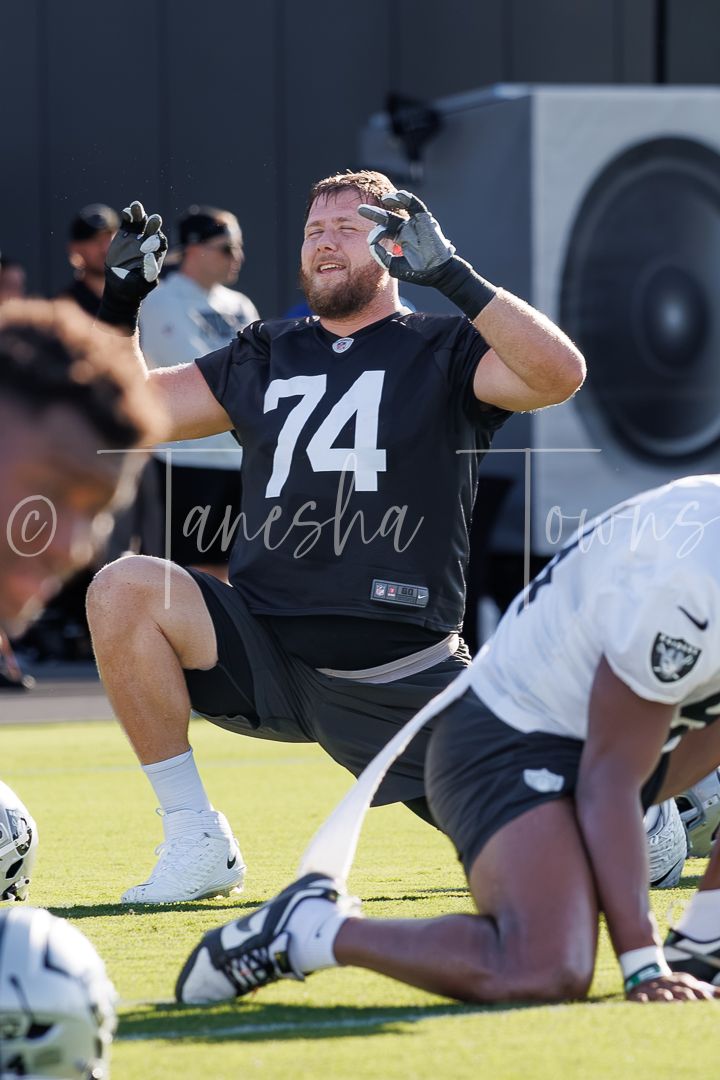 NFL player #74 stretching on field during Raiders training camp practice in black jersey and gloves.
