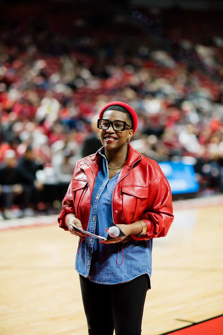 A person in a red leather jacket and denim shirt performs at a sporting event.