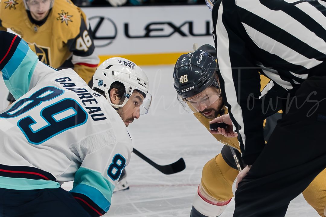 NHL hockey players battle for possession during an intense game with referees watching closely.