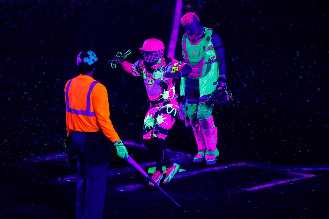 Athletes celebrate in vibrant neon outfits glowing under black lights at a nighttime event.