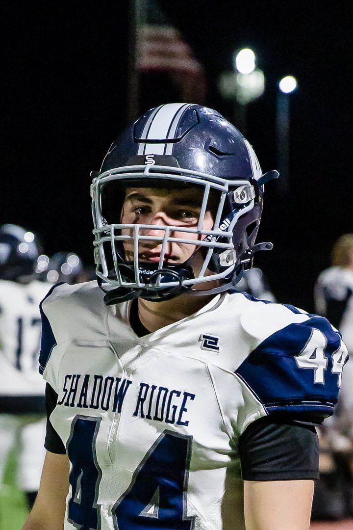 Football players in white uniforms with Shadow Ridge branding stand on sideline.