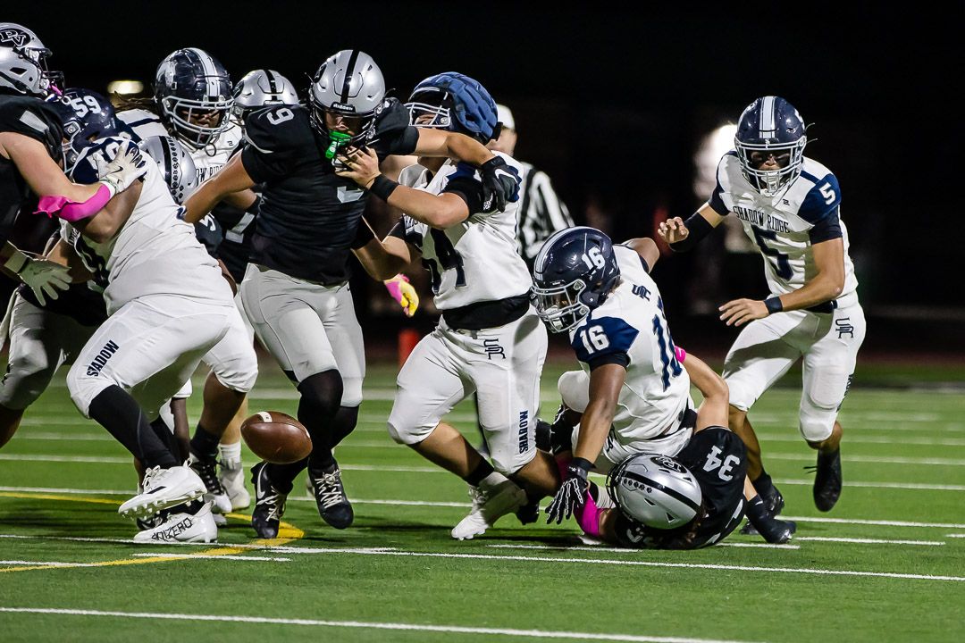 Players from opposing teams collide in a chaotic pile-up during a nighttime football match.